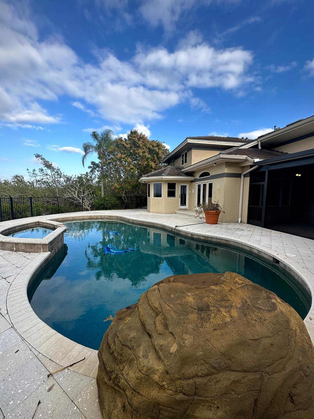 Backyard pool and spa with travertine paver deck beside a repainted two-story home