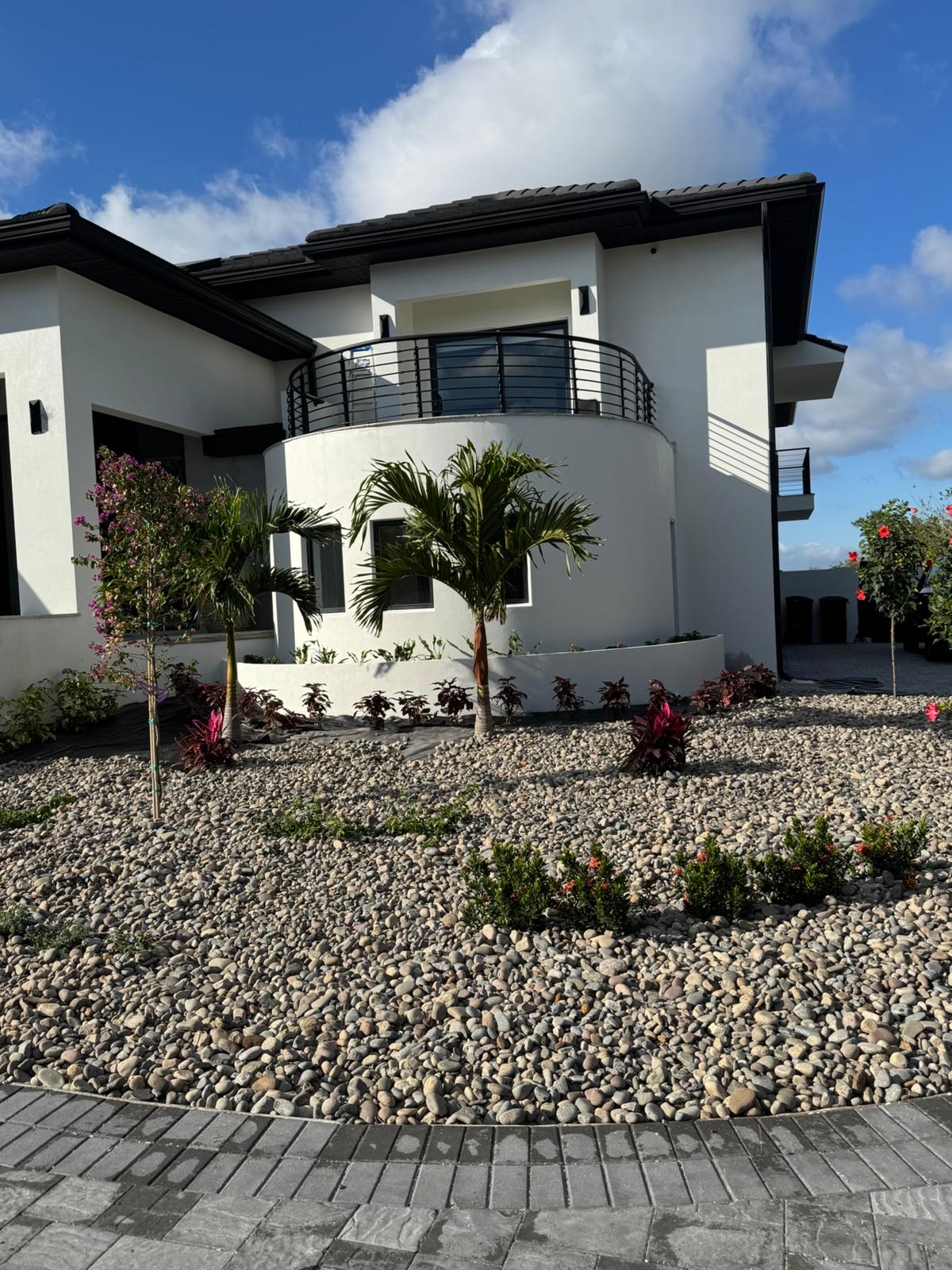 Front corner of white home with palms, river rock beds and paver drive