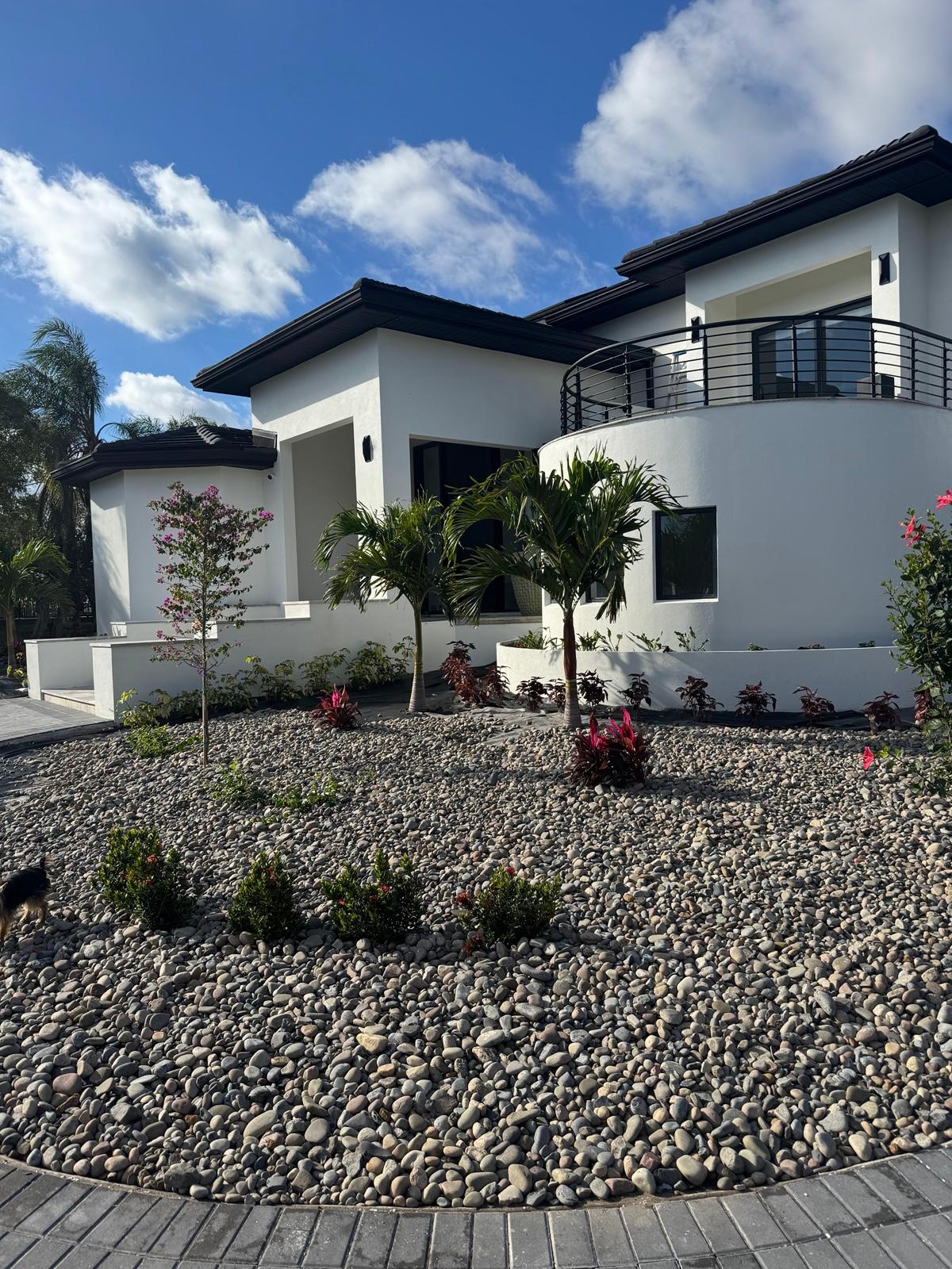 White stucco front elevation with curved balcony and river rock landscaping