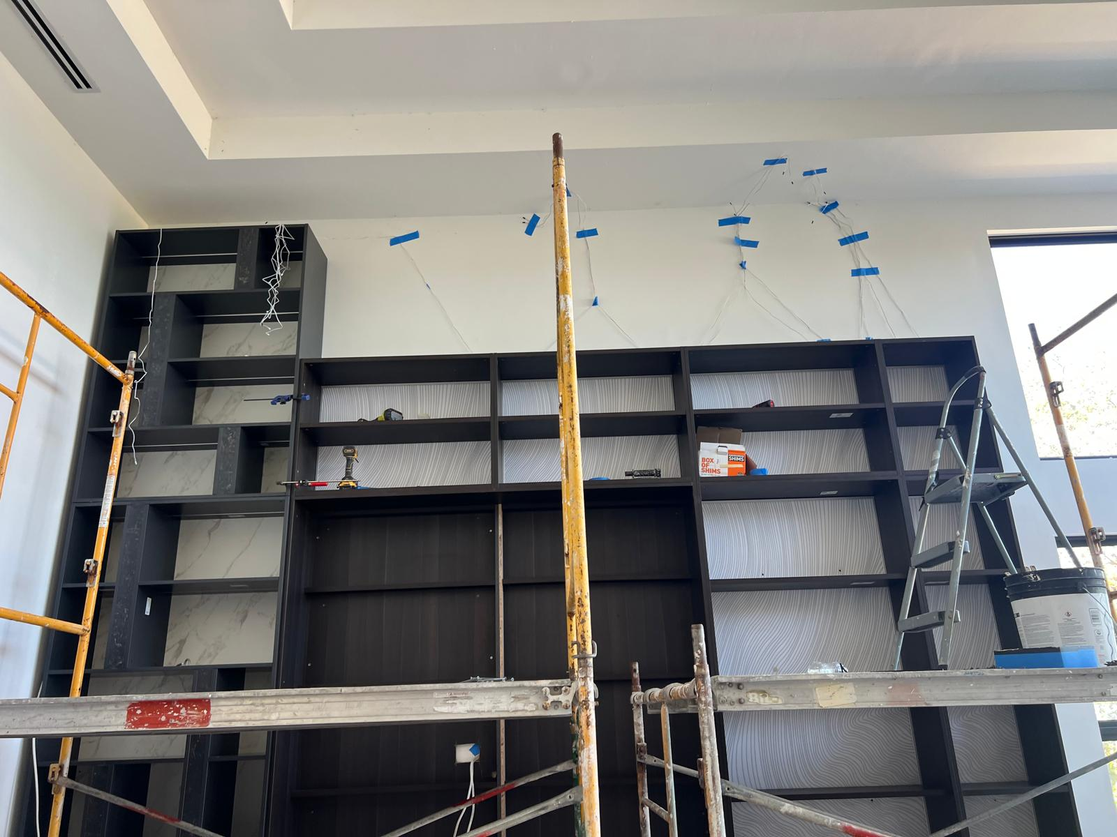 Floor-to-ceiling black built-in shelving with marble accent panels mid-install