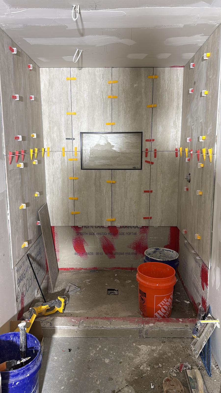 Large-format travertine shower tile install with leveling clips and niche framing
