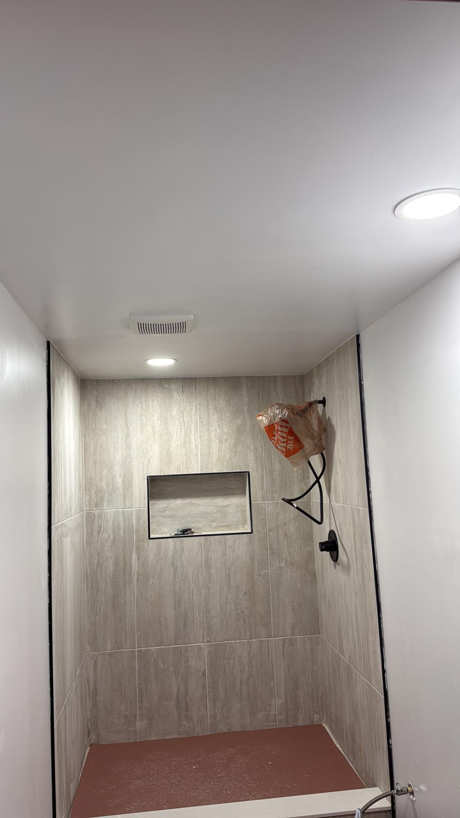 Finished travertine tile shower with black-framed niche and matte black fixtures