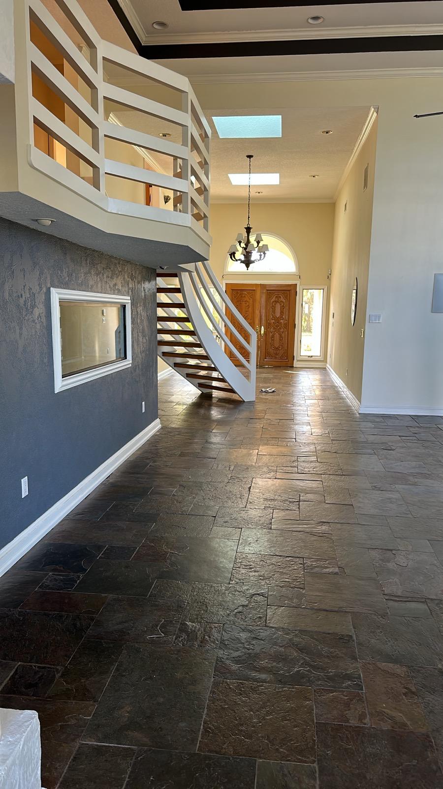 Open hallway with slate tile flooring, curved staircase and accent plaster wall