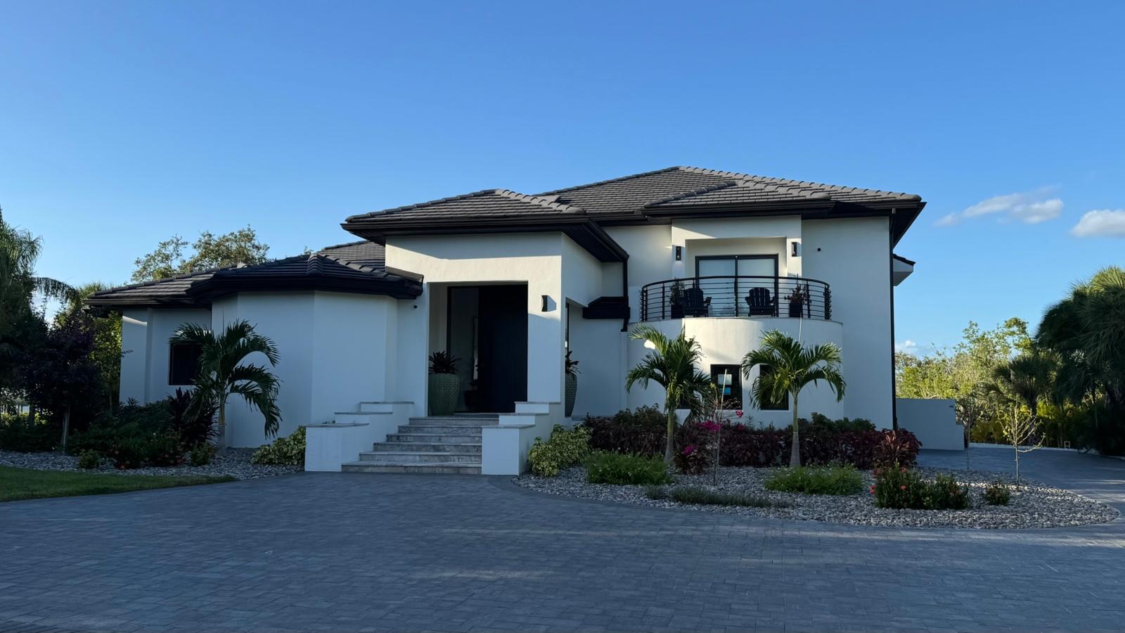 White stucco home front elevation with tile roof, balcony and paver driveway