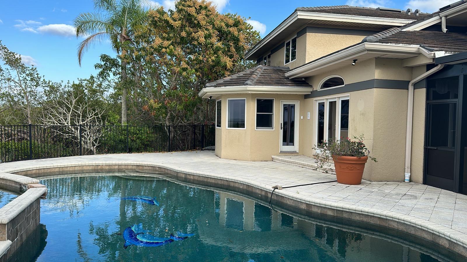 Pool and paver deck beside a two-story home with screened lanai