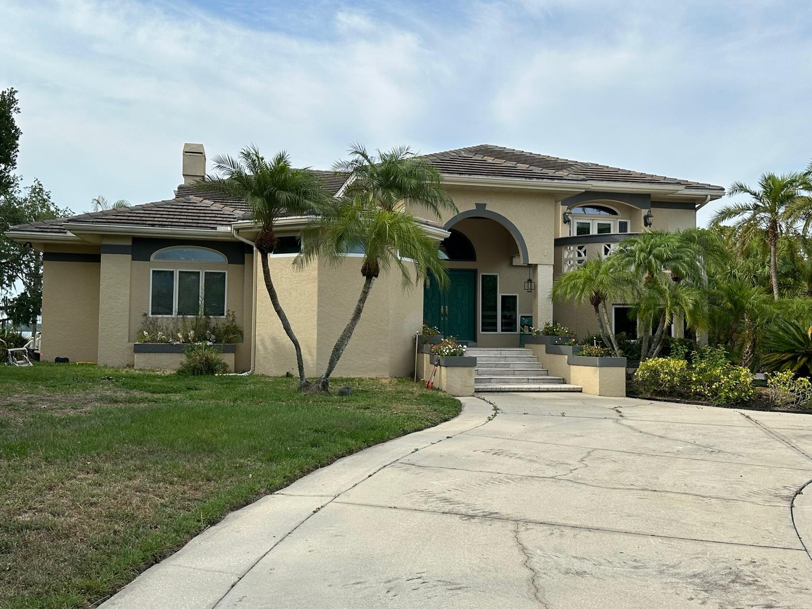 Tan stucco two-story home with palms before exterior renovation