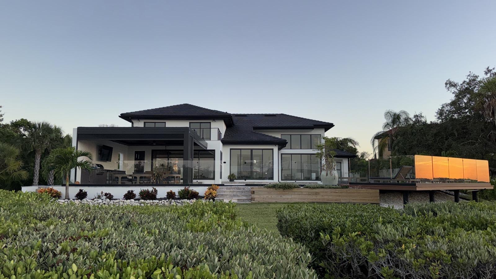Wide rear view of a modern white home at dusk with landscaped yard and deck