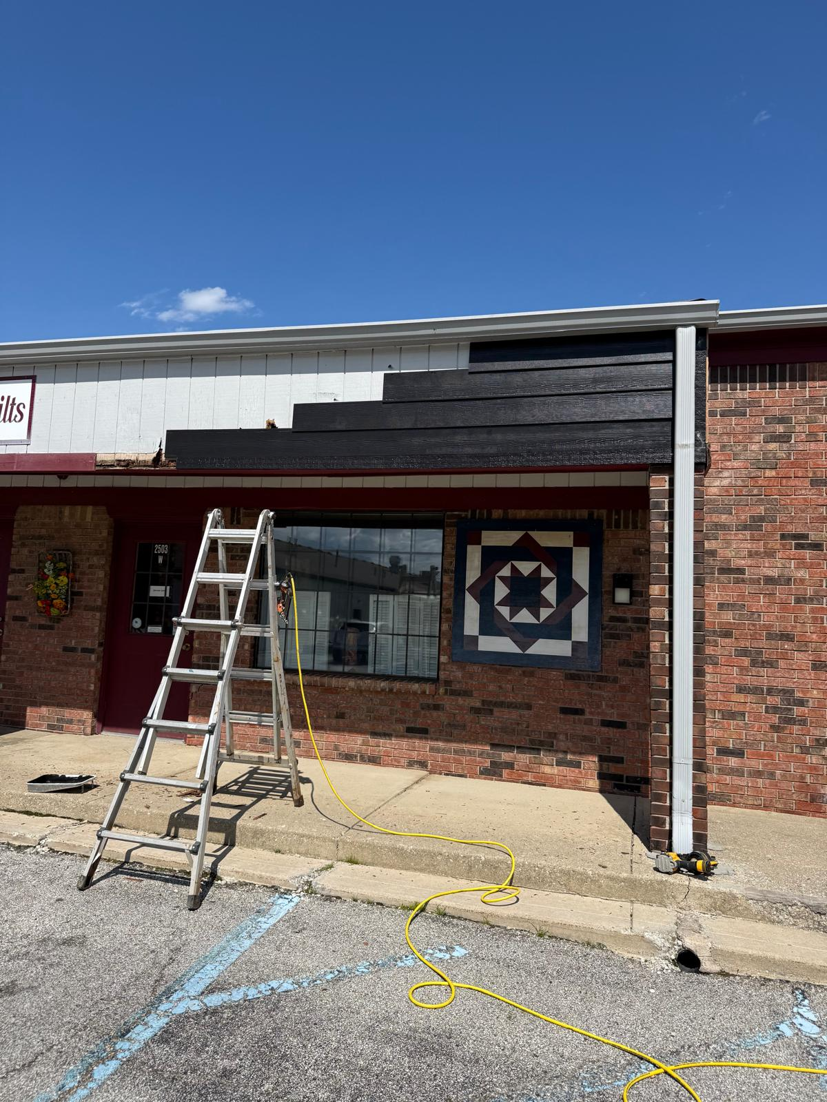 Commercial exterior siding mid-repaint with ladder and fresh dark coat
