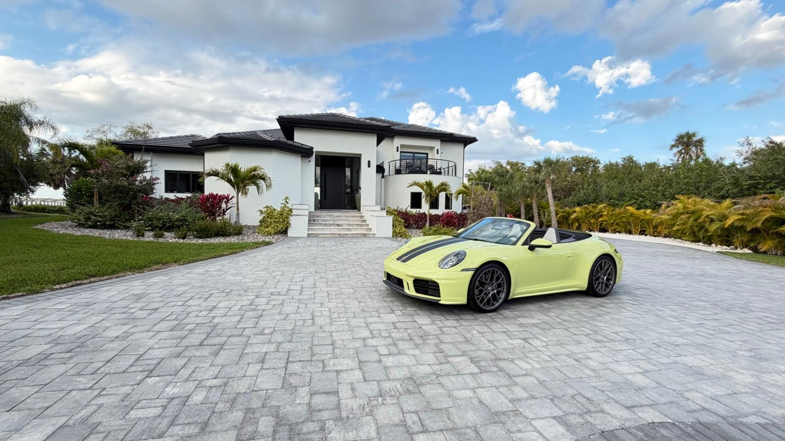 Modern white stucco home with dark trim, paver driveway and tropical landscaping