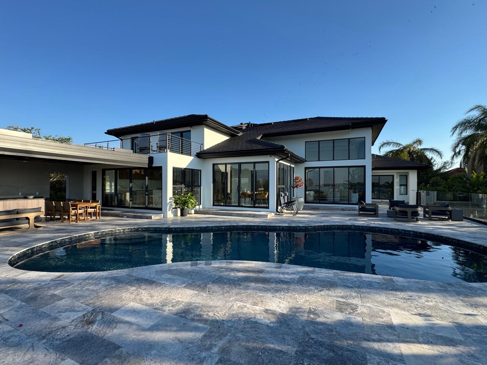 Wide rear view with pool, covered outdoor kitchen and black-framed glass doors