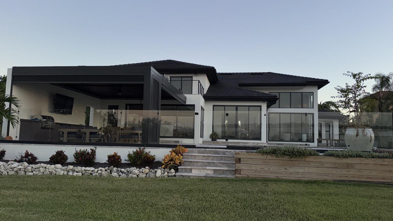 Rear elevation at dusk with covered outdoor kitchen and glass railing