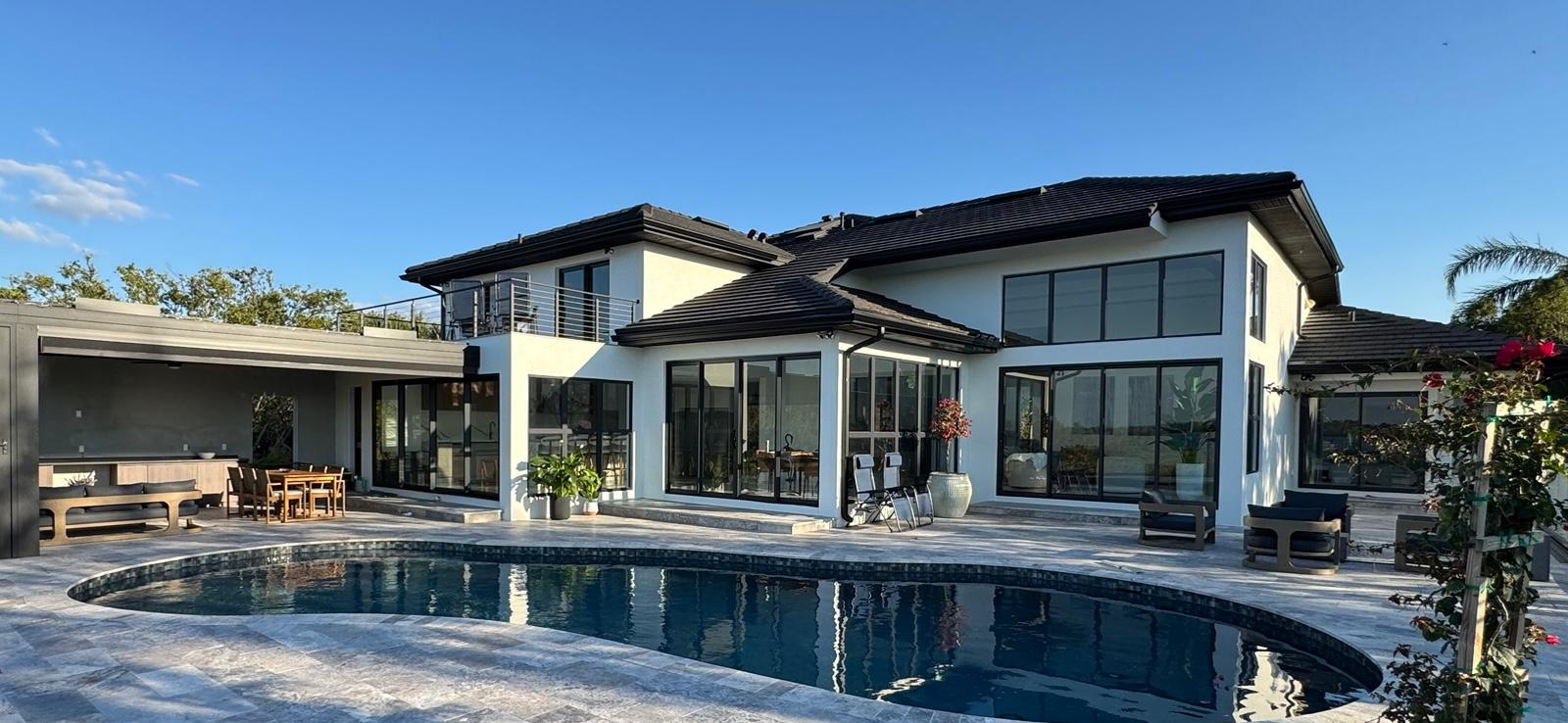 Finished white home rear elevation with pool, travertine deck and outdoor kitchen