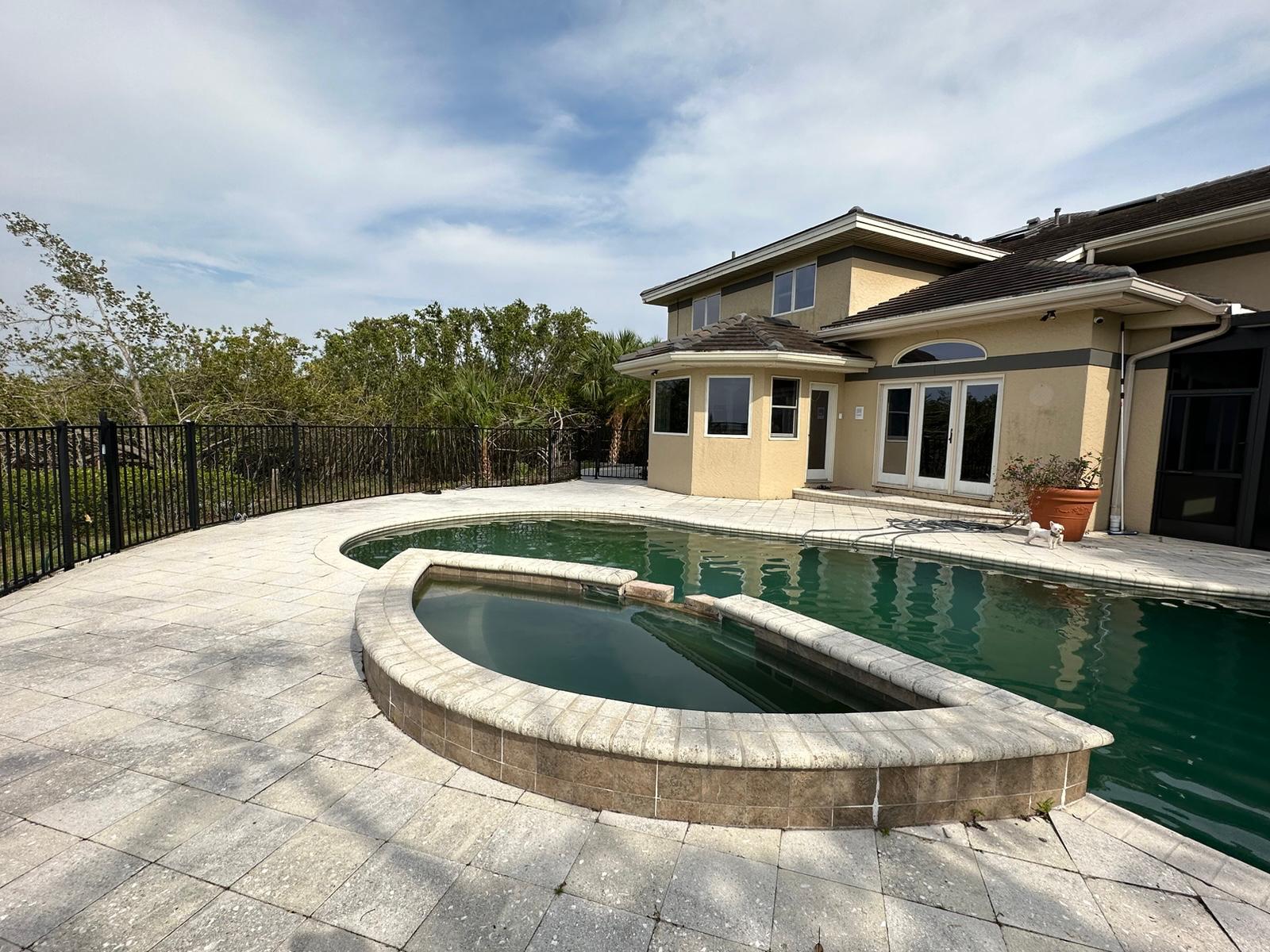 Wide pool and spa deck with dated pavers before resurfacing